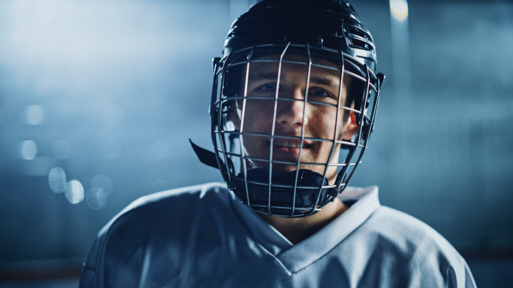 Ice Hockey Arena: Portrait of Confident Professional Player, Wearing Wire Cage Face Mask, Looking at Camera and Smiling. Close-up Shot