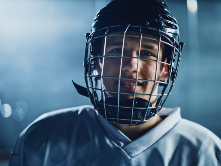 Ice Hockey Arena: Portrait of Confident Professional Player, Wearing Wire Cage Face Mask, Looking at Camera and Smiling. Close-up Shot