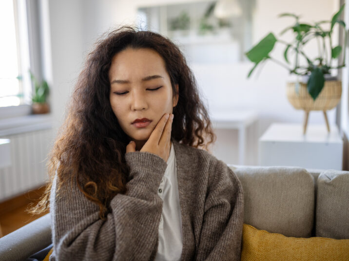 Portrait of unhappy young Asian woman suffering from toothache at home. Healthcare, dental health and problem concept.