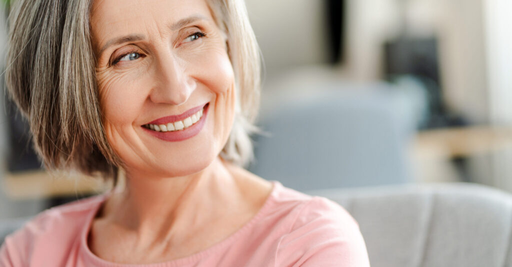 Smiling confident senior woman sitting on comfortable sofa at home. Happy female looking away