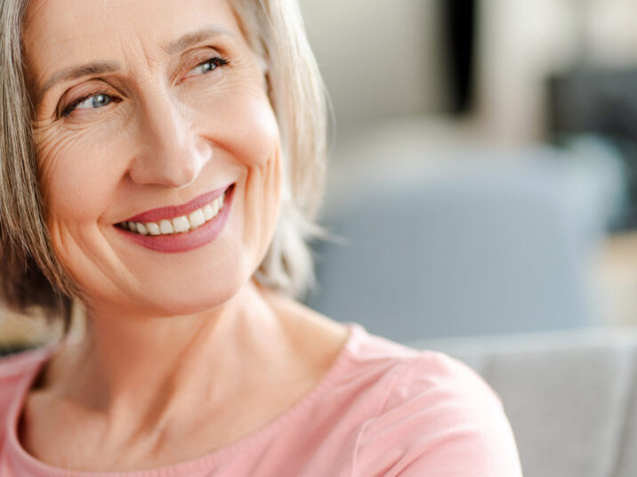 Smiling confident senior woman sitting on comfortable sofa at home. Happy female looking away