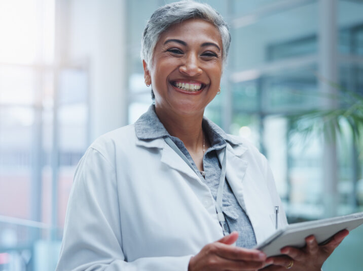 Female doctor, portrait and smile with tablet in hospital or workplace with lens flare. Communication, technology and medical research for innovation in medicine with happy healthcare professional.