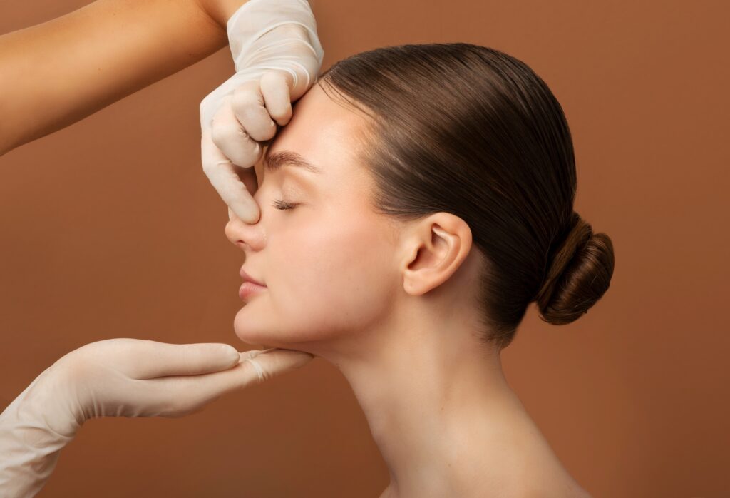 Surgeon touching woman nose, consulting lady before rhinoplasty operation, brown studio background, side view. Plastic surgery concept